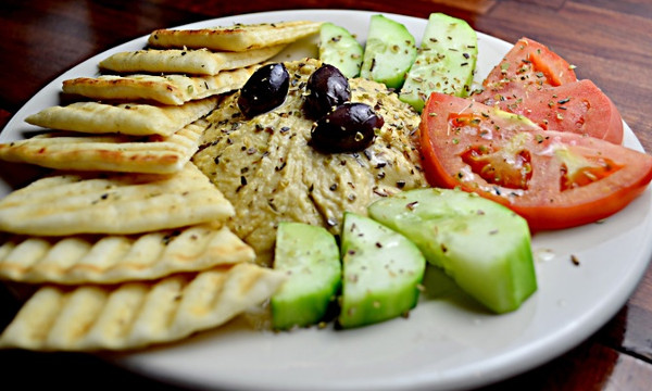 Fotografi av pitabrød dandert på en asjett med friske grønnsaker og hummus.